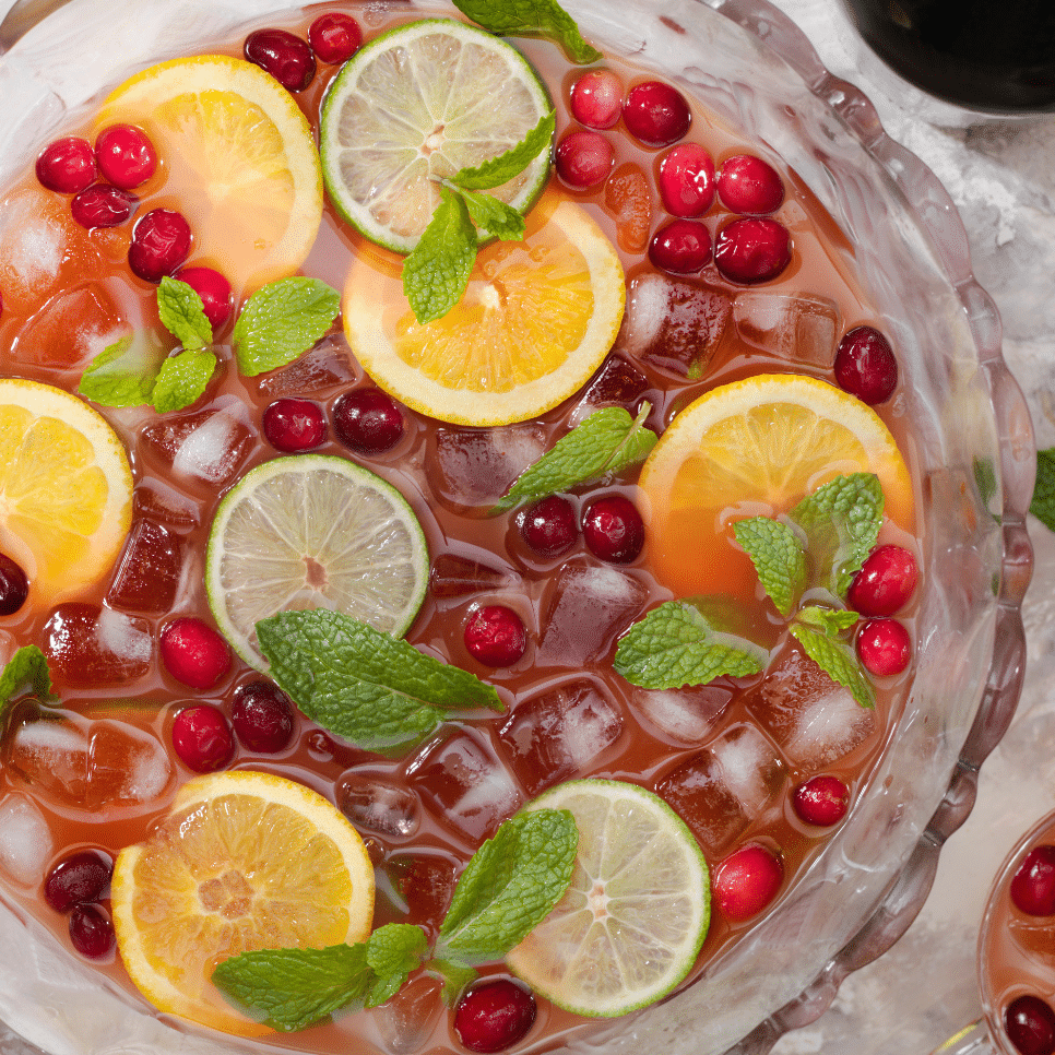 Punch bowl with fruit slices, cranberries, mint, and ice.
