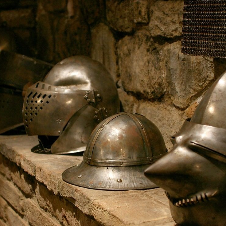 Medieval helmets on a stone shelf against a stone wall.