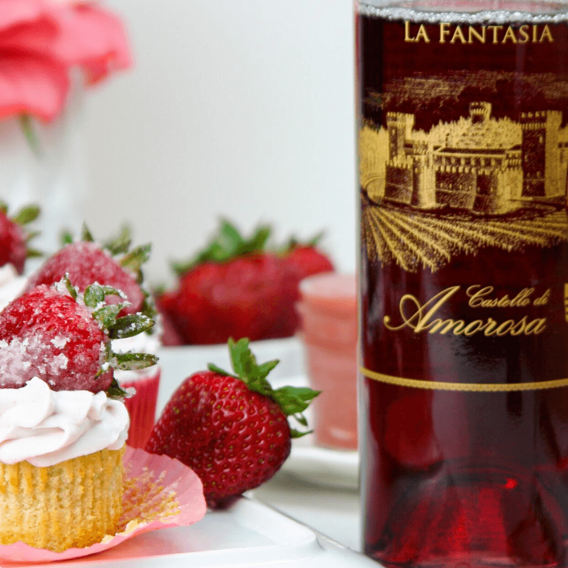 Bottle of red wine, cupcakes, and strawberries in a bright setting.