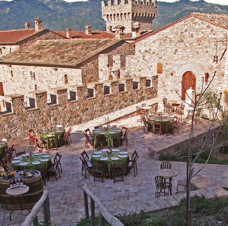Outdoor courtyard restaurant with round tables, a stone castle backdrop, and mountain view.