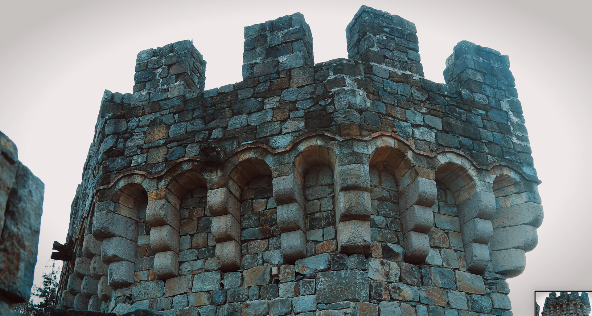 Stone castle tower with crenelated top and arched openings.