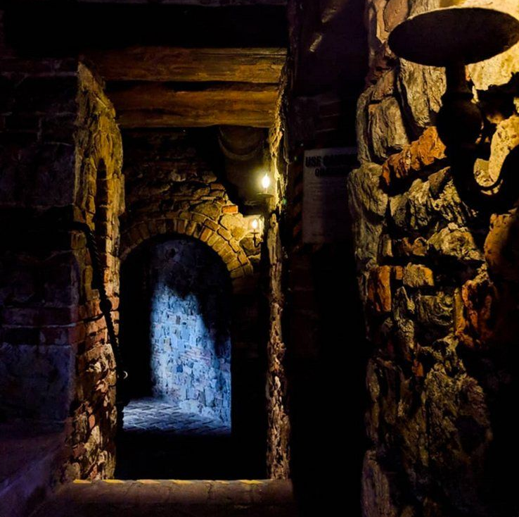 Stone passageway with arched doorways, dimly lit by sconces. Dark, old interior.