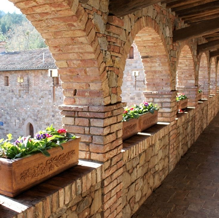 Brick arches and flower boxes line a stone walkway overlooking a building.
