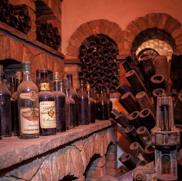 Wine cellar with dusty bottles on brick shelves and arched alcoves.