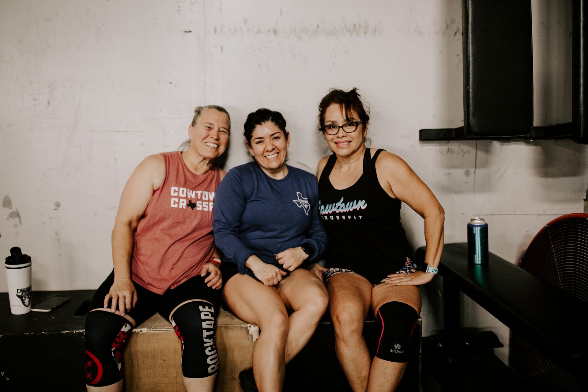 Three women are sitting next to each other on a bench in a gym.
