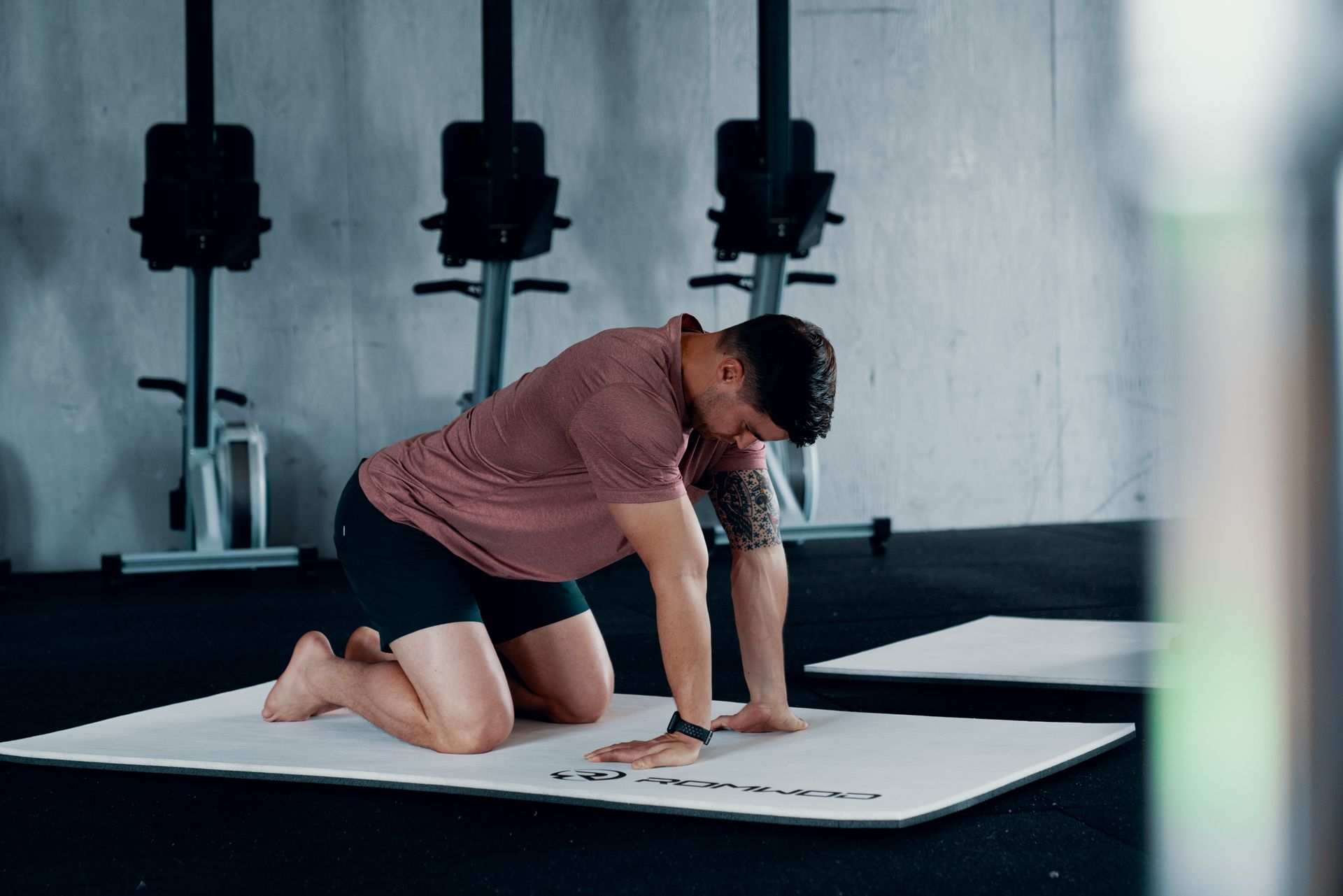 A man is kneeling on a yoga mat in a gym.