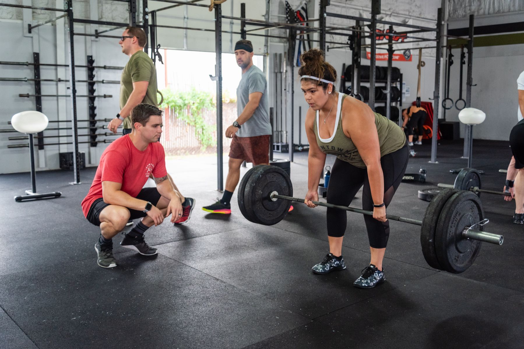 A woman is lifting a barbell in a gym while a man watches.