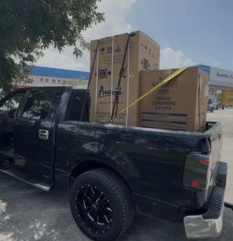 Black pickup truck bed loaded with two large boxes, secured with straps, parked outside a store. Black pickup truck bed loaded with two large boxes, secured with straps, parked outside a store.