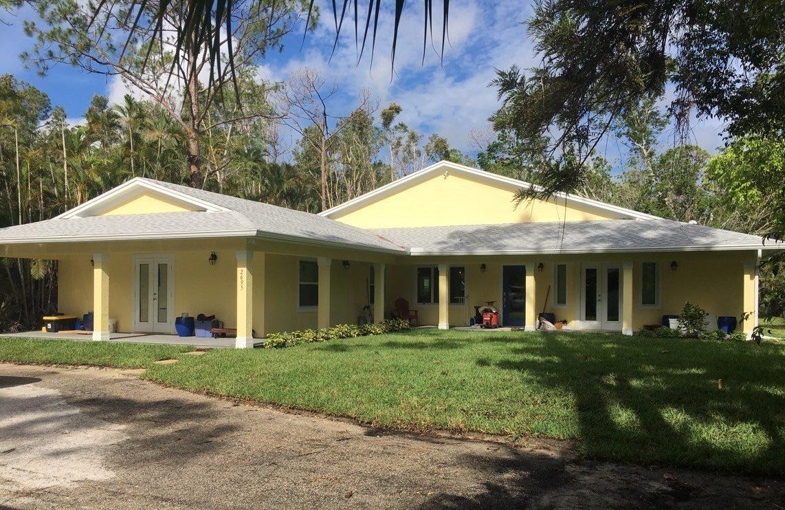 A large yellow house with a white roof is surrounded by trees.