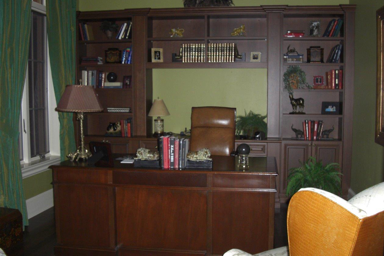 A living room with a desk, chair, lamp and bookshelves.