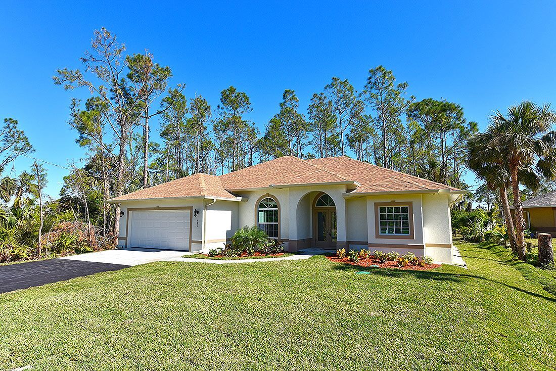 A white house with a brown roof is sitting on top of a lush green lawn.