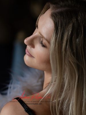 Woman with blonde hair, looking up with closed eyes. Shoulder in focus, dark background.