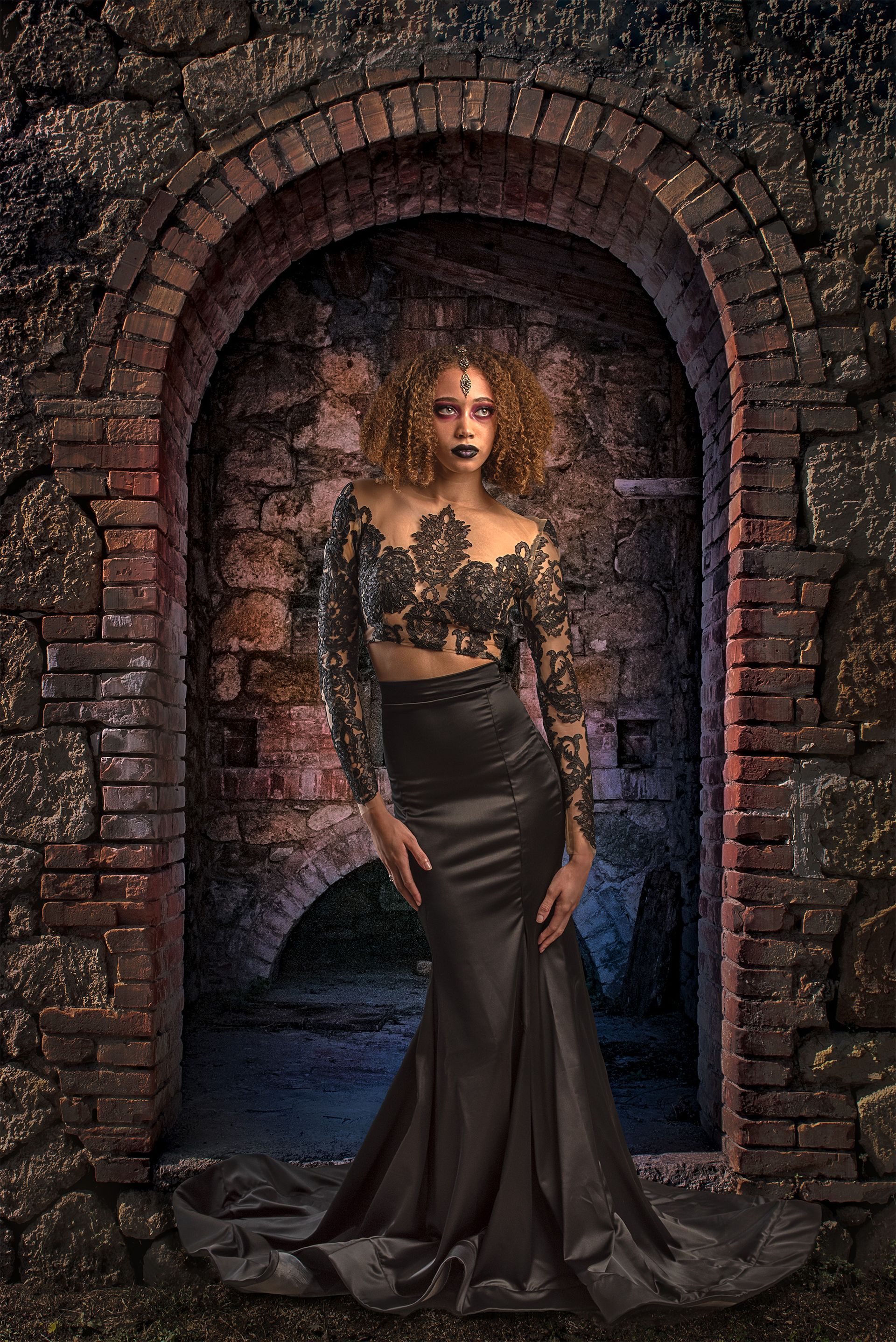 Woman in black formal attire, posing in arched brick doorway.