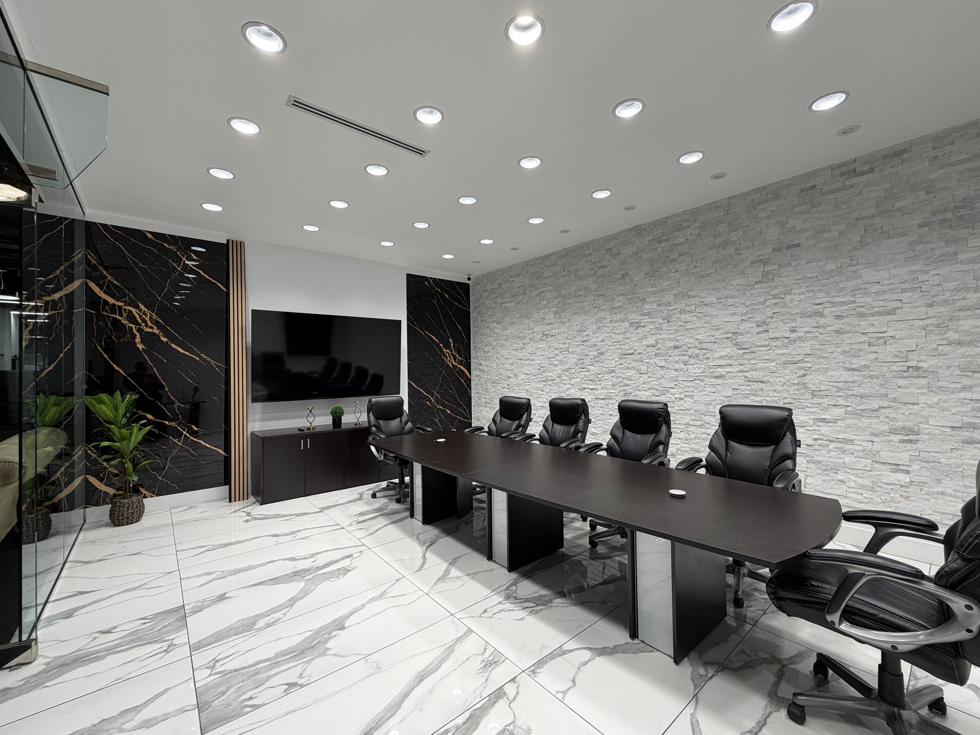 Modern open office with glass walls, desks, lounge seating, and black ceiling lights