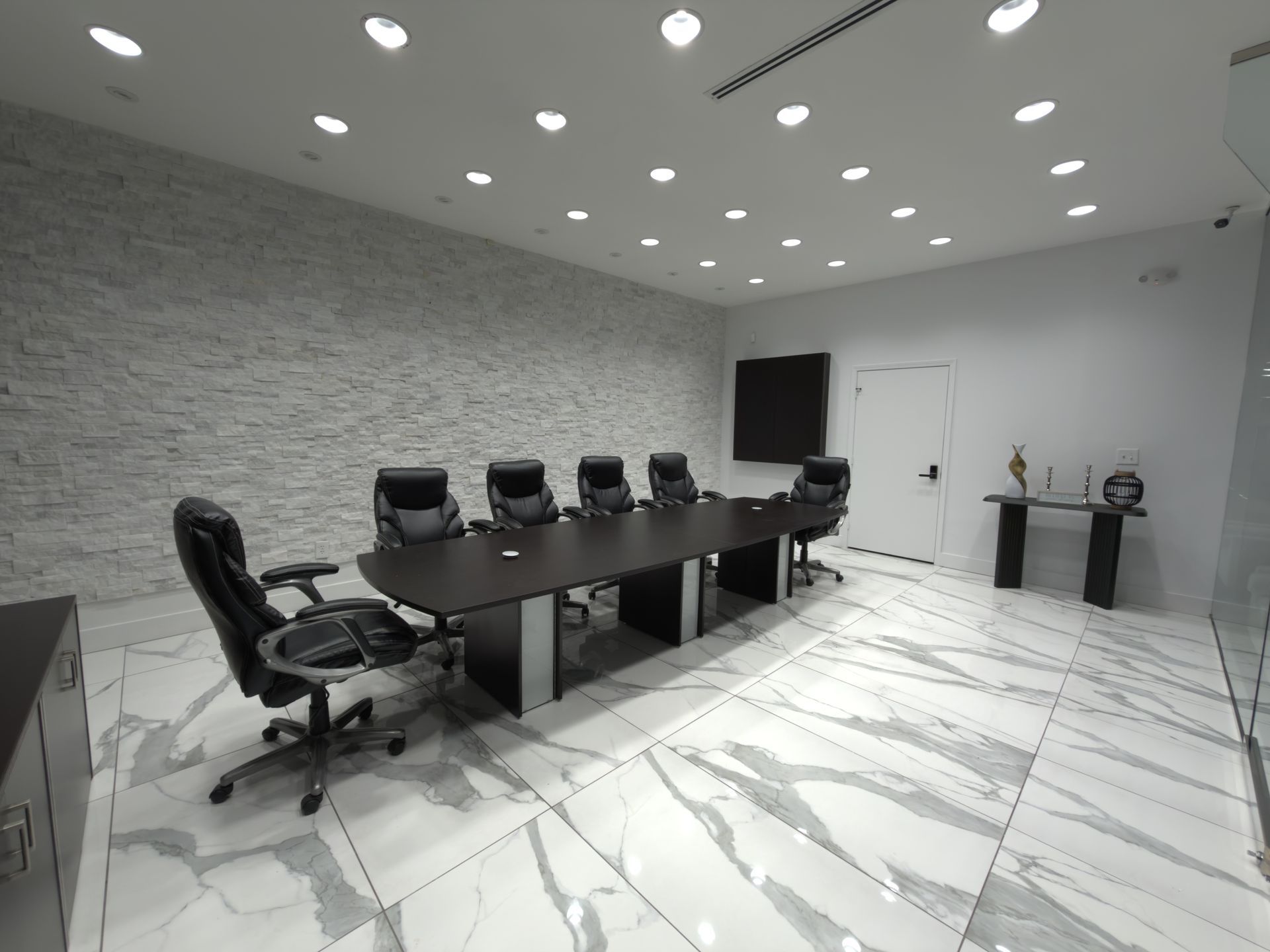 Modern conference room with black chairs, long table, wall-mounted TV, and white marble floor.