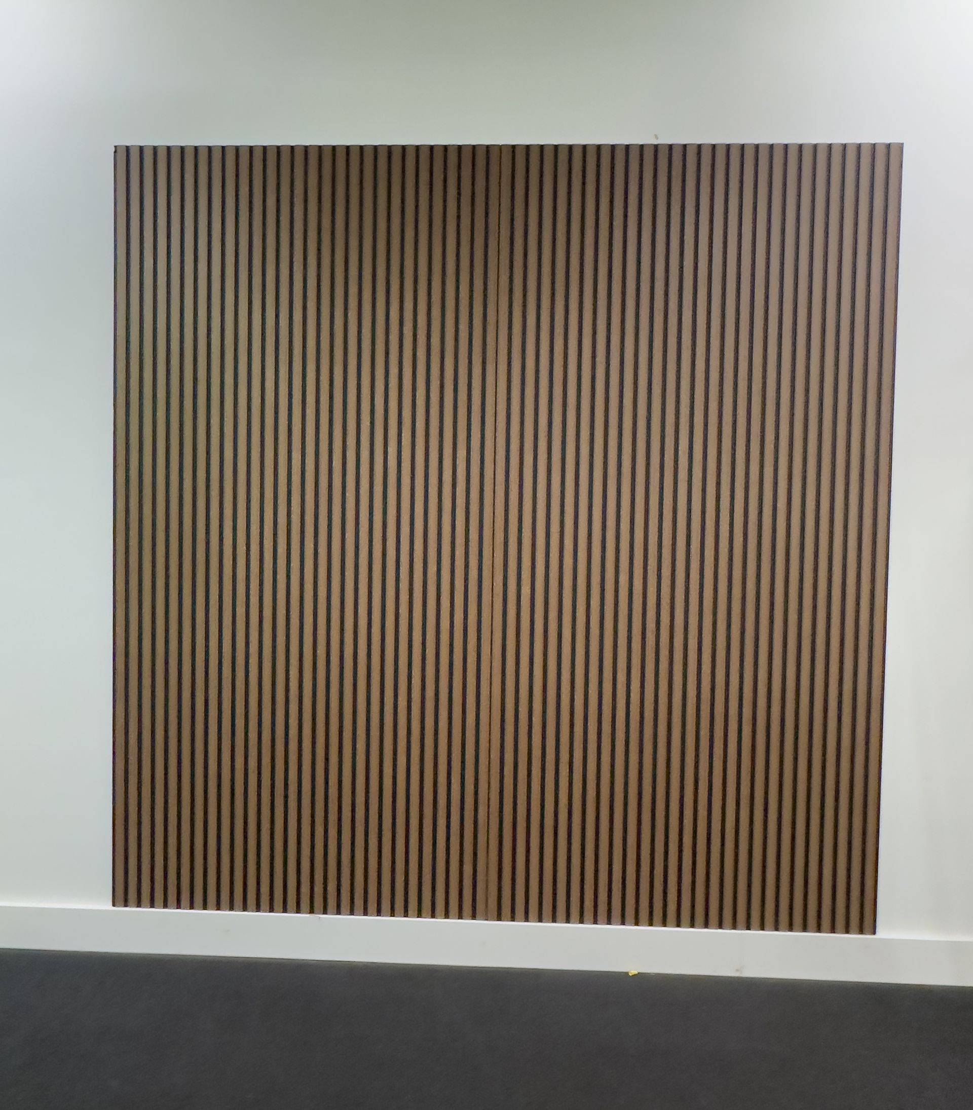 Laptop with editing software, camera, and tablet on a wooden table in a bright office. People in the background.