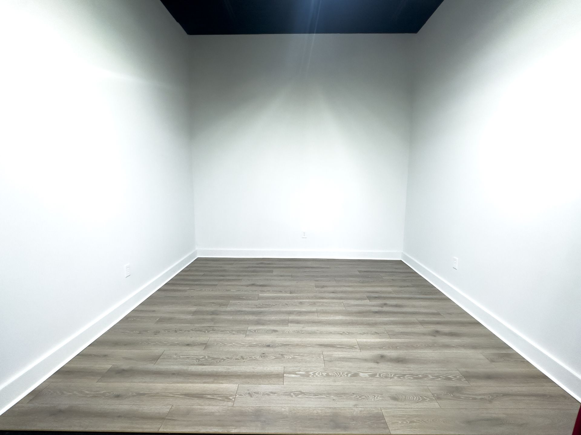 Long, pink hotel hallway with doors on both sides, leading to a distant door with light.