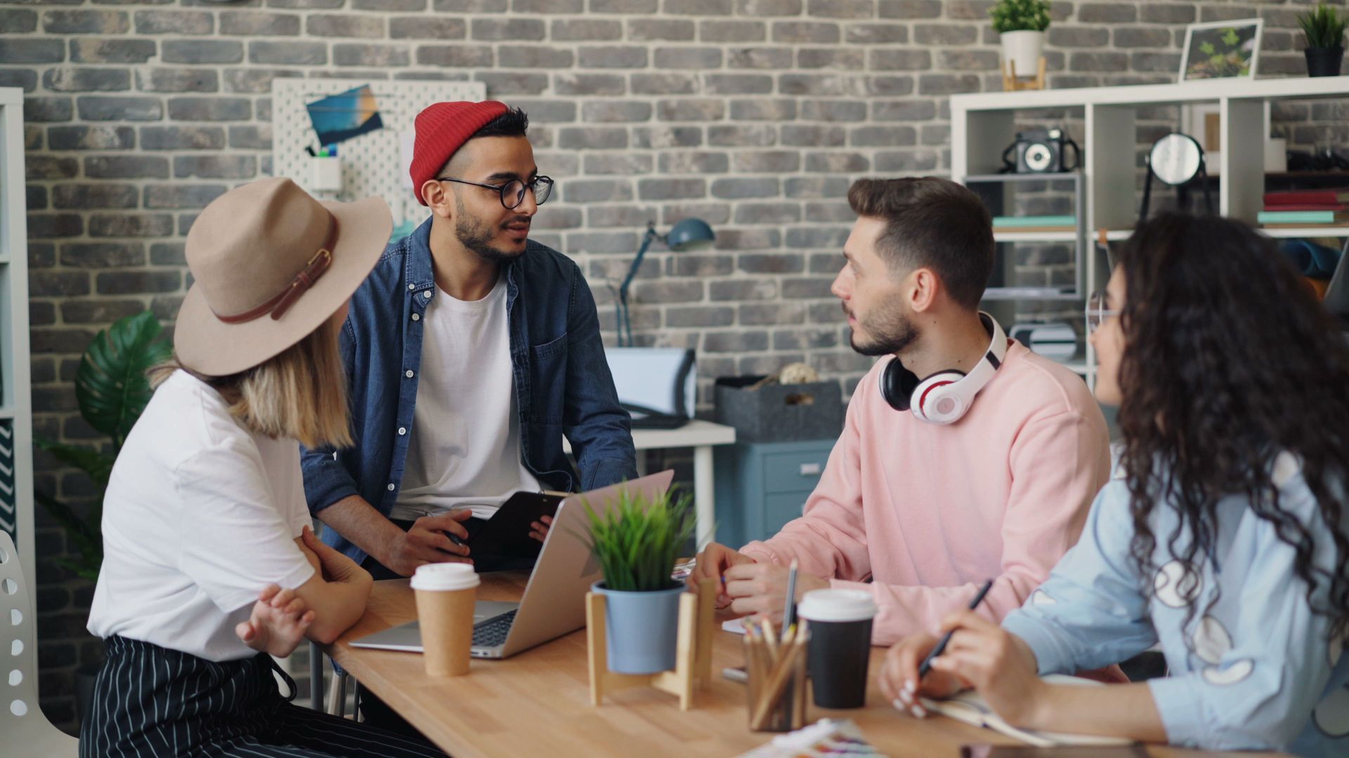 Coworkers chatting around a laptop at a table in a casual office lounge