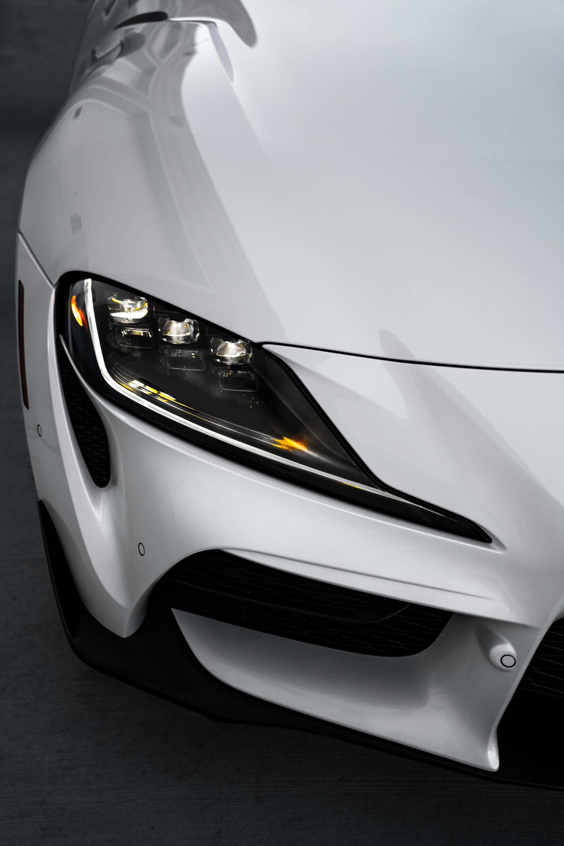 White sports car, front view. Headlight detail, sleek design, against a dark background.