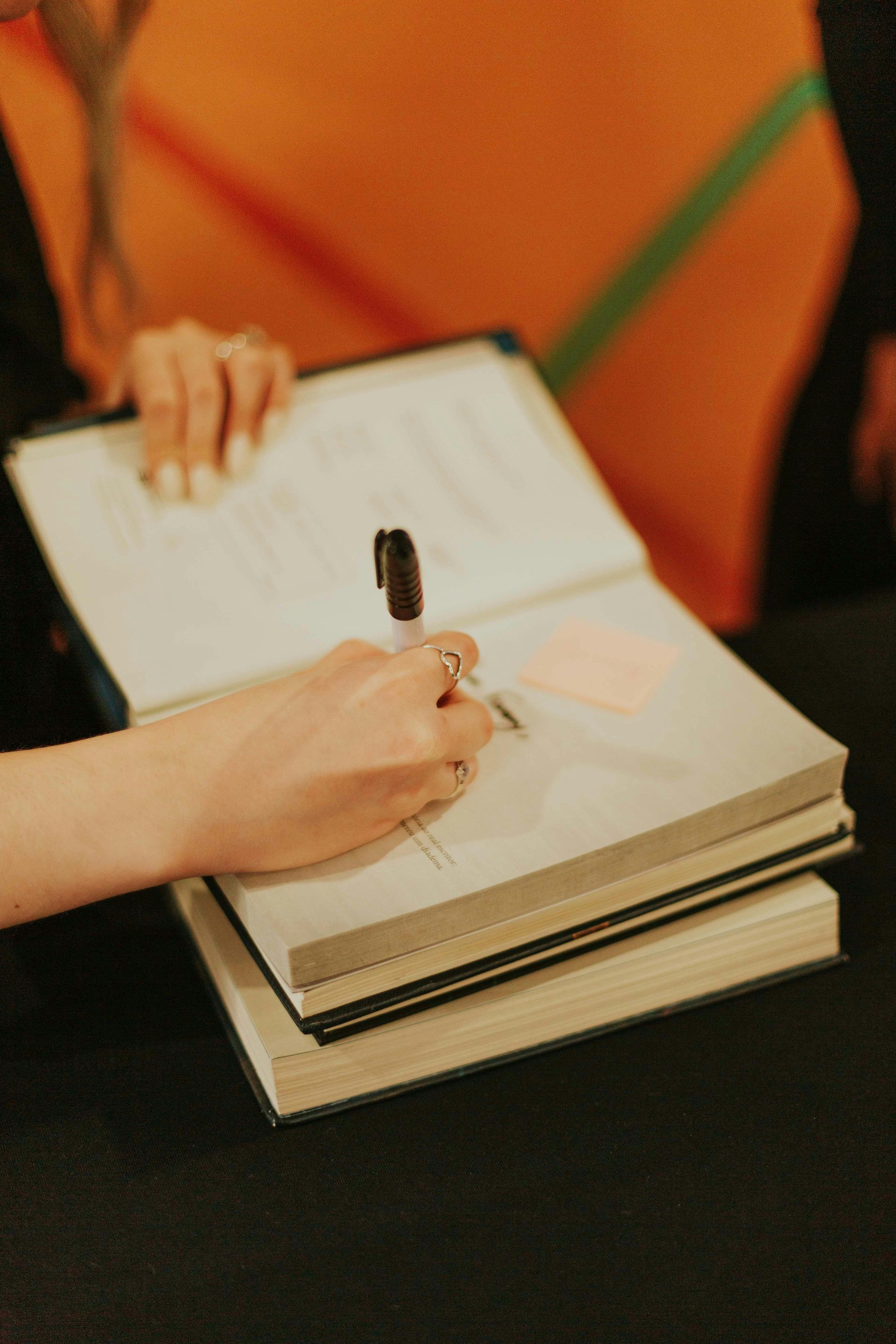 Hand writing in a notebook on a stack of books at a table