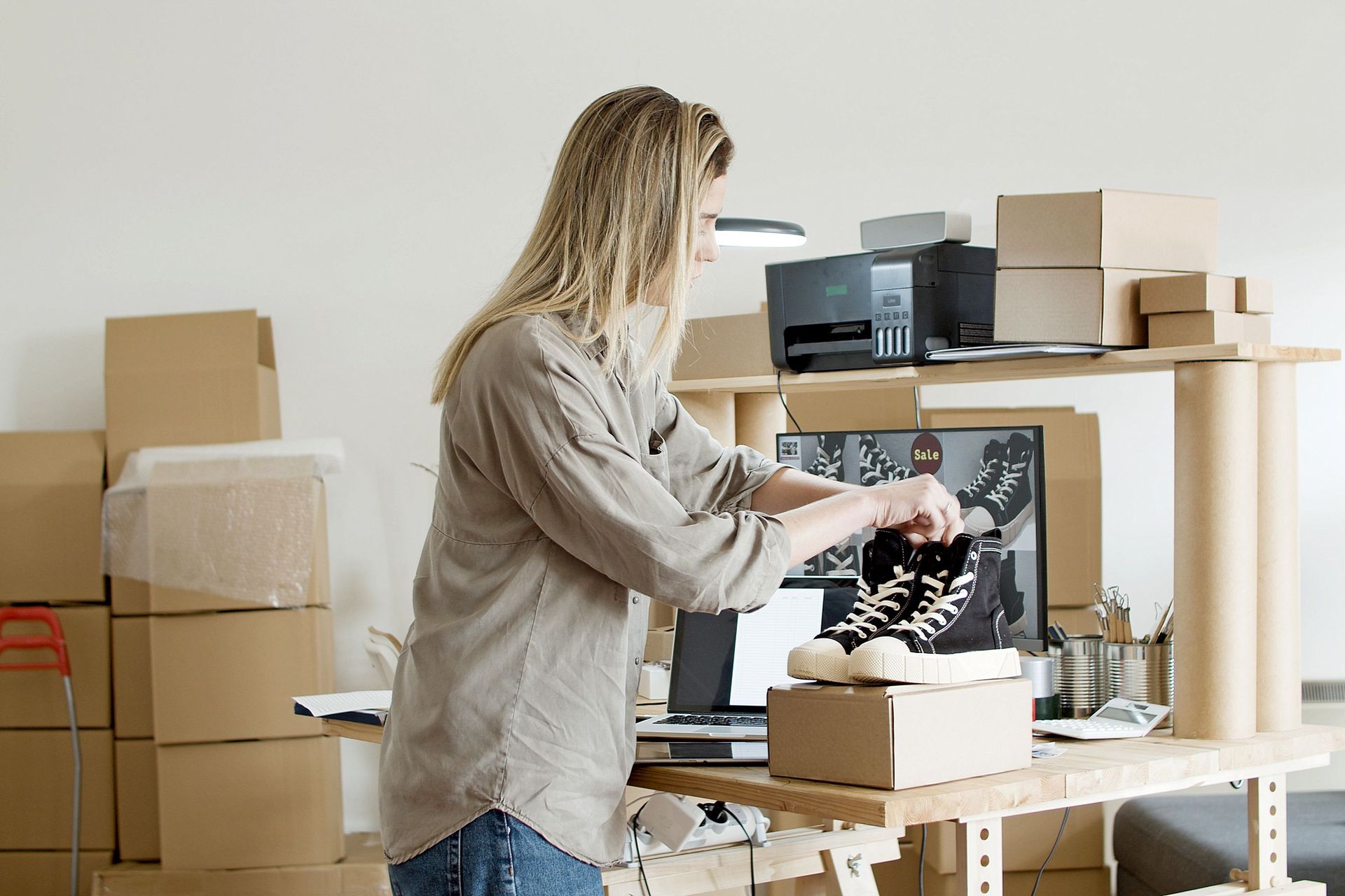 Person packing items into a box in a home office with stacked moving boxes