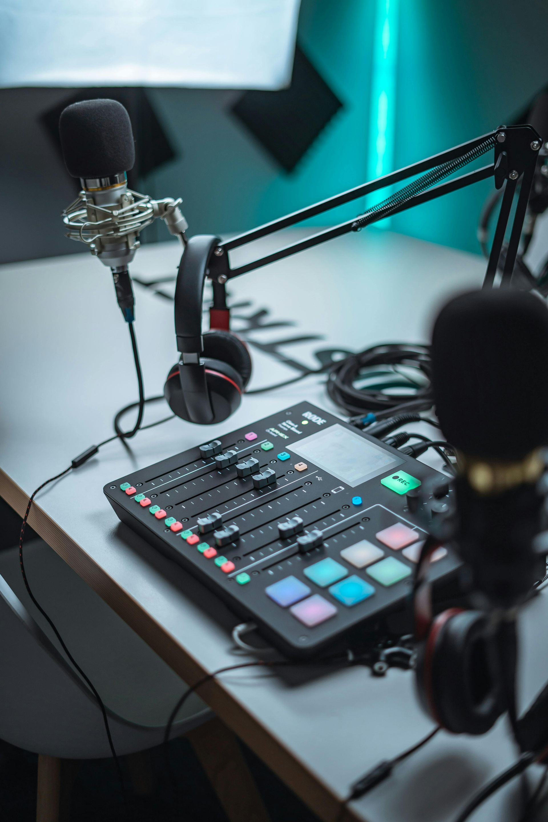 Podcast studio setup with microphones, audio mixer, headphones, and cords on a white desk.