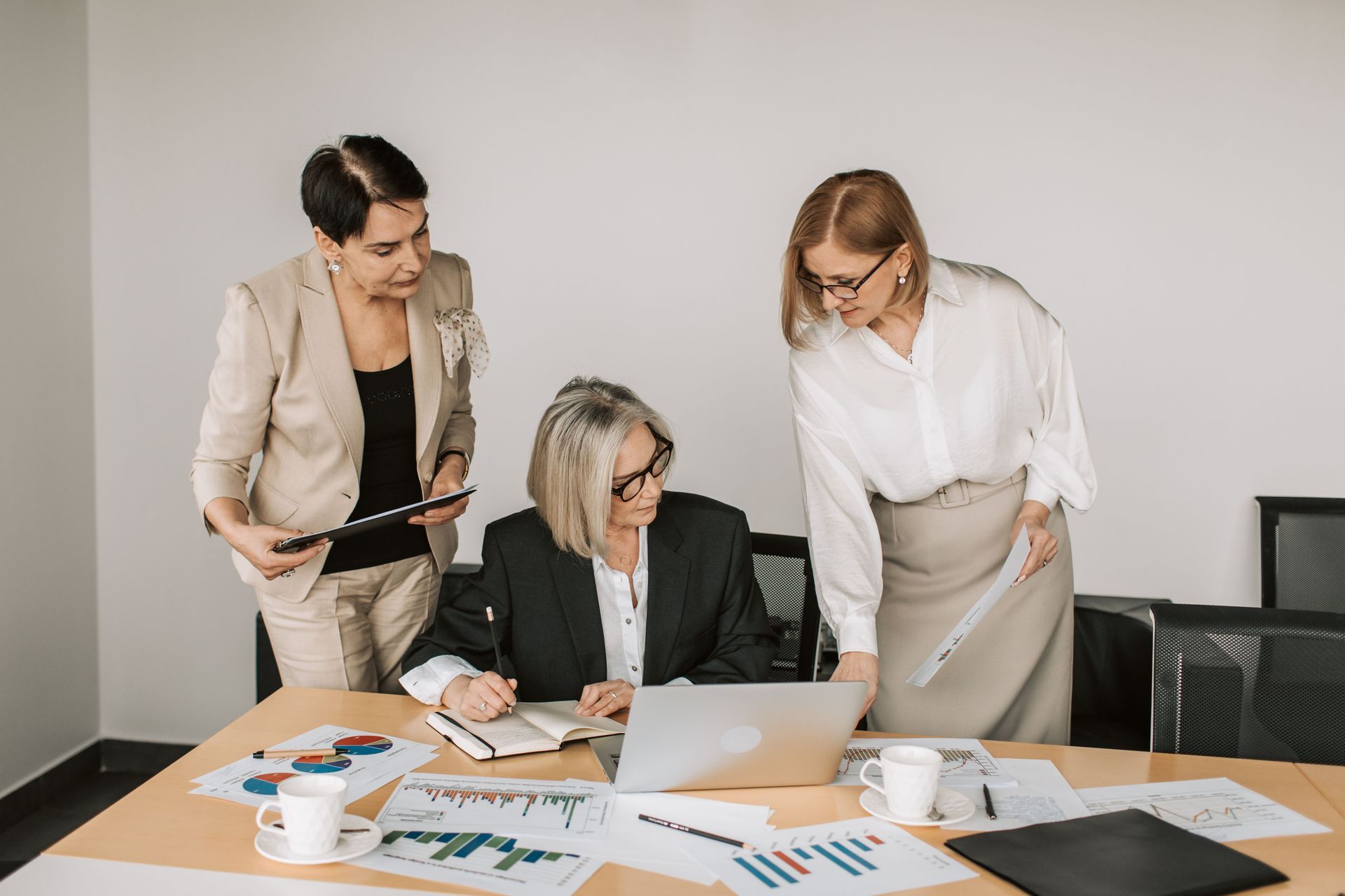 Three coworkers review charts and a laptop at a conference table in a bright office