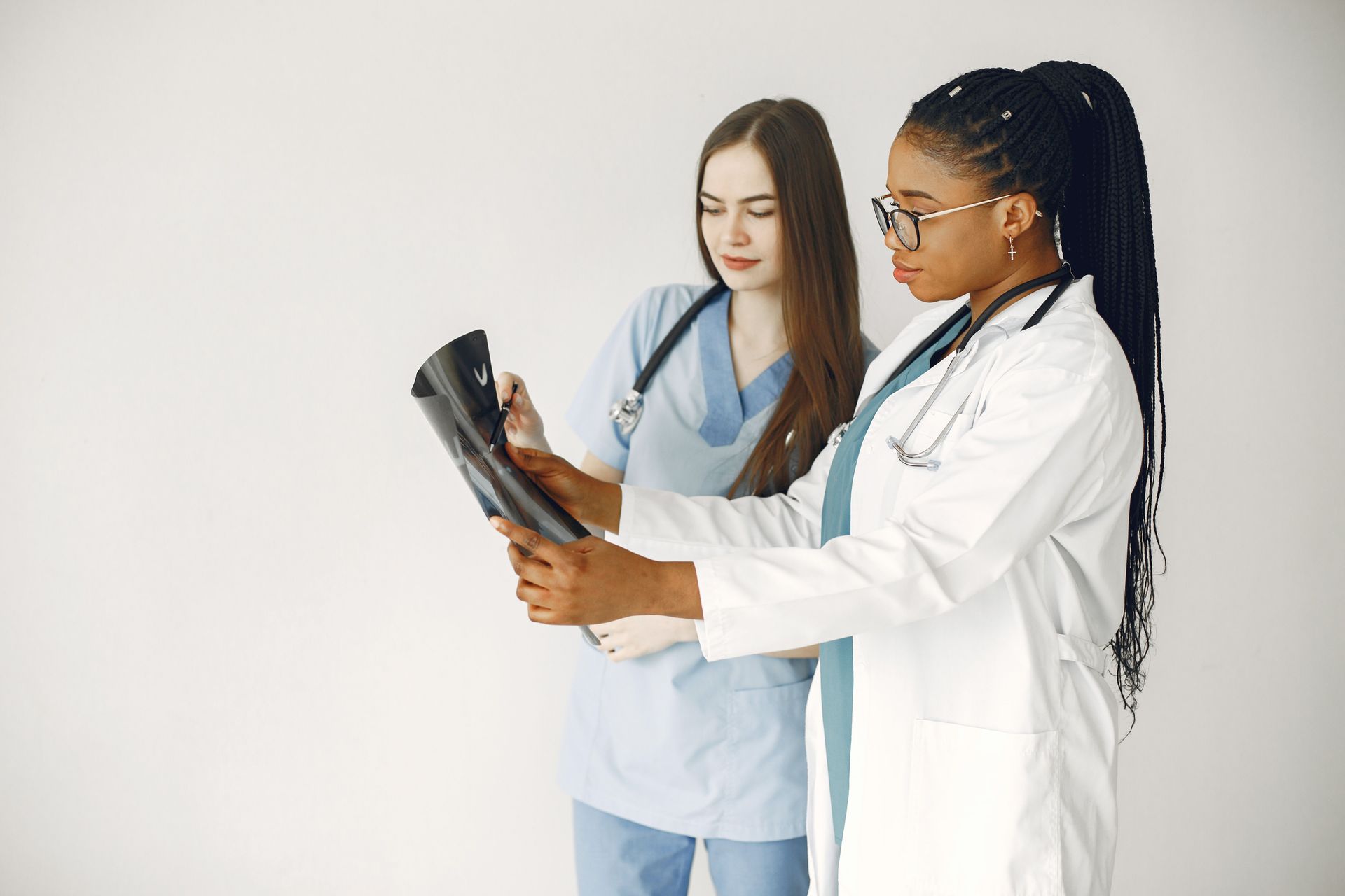 Two medical professionals in white and blue scrubs reviewing X-ray films together