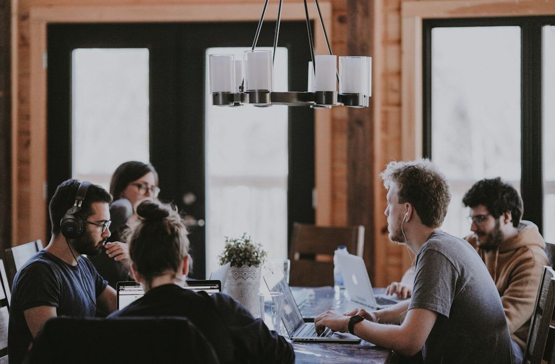 People gathered around a table in a bright office meeting room with large windows and a hanging light fixture.