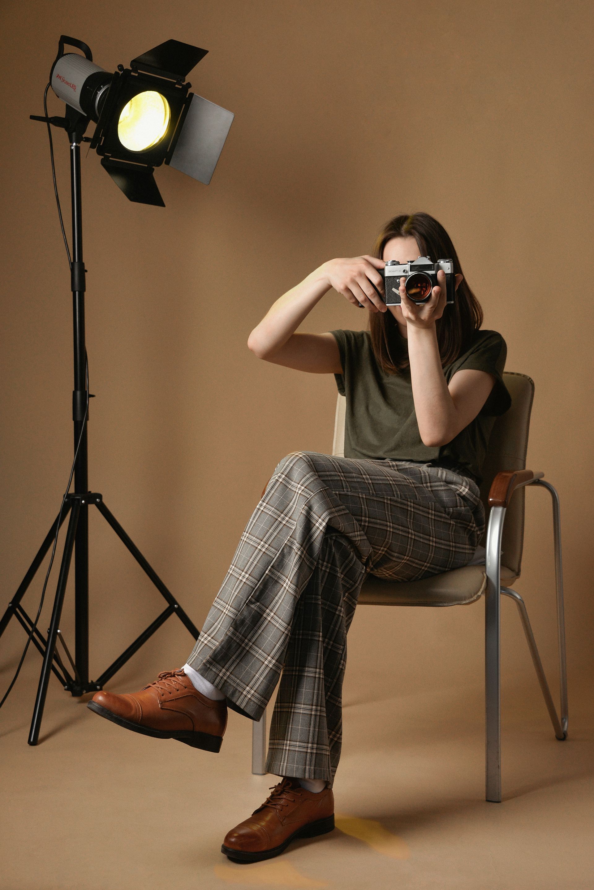Woman seated, taking photo with vintage camera; studio lighting.