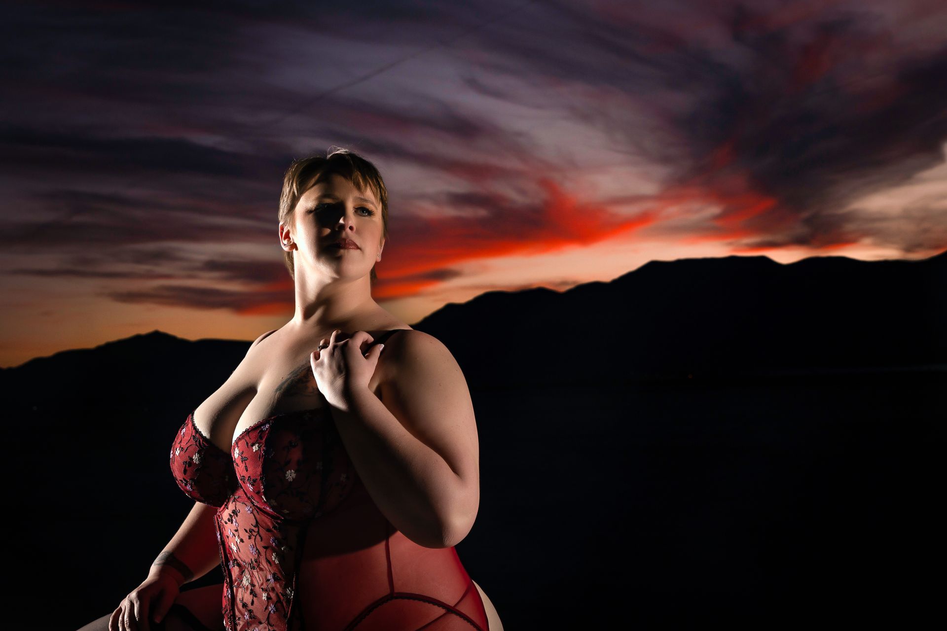 Woman in red corset against mountain silhouette at sunset with dramatic clouds