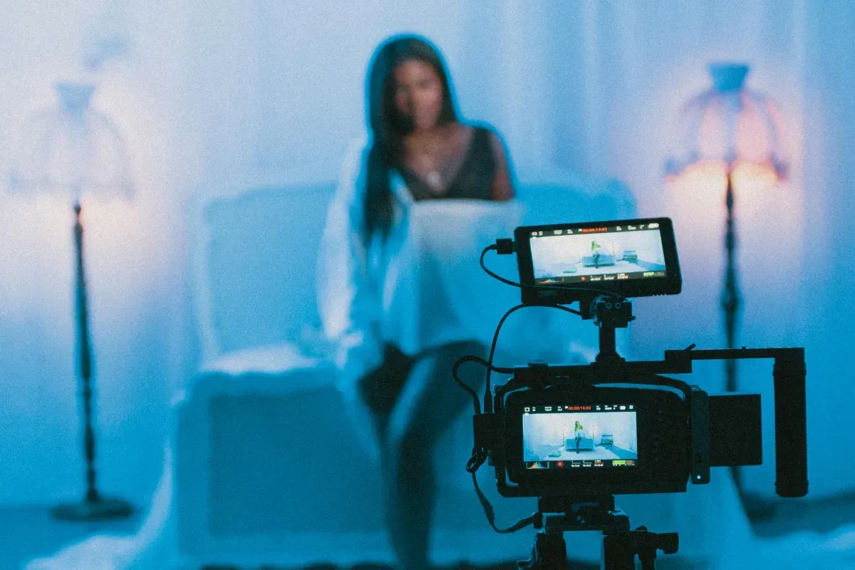 Woman posing in a blue-lit studio while a camera records her on a monitor display