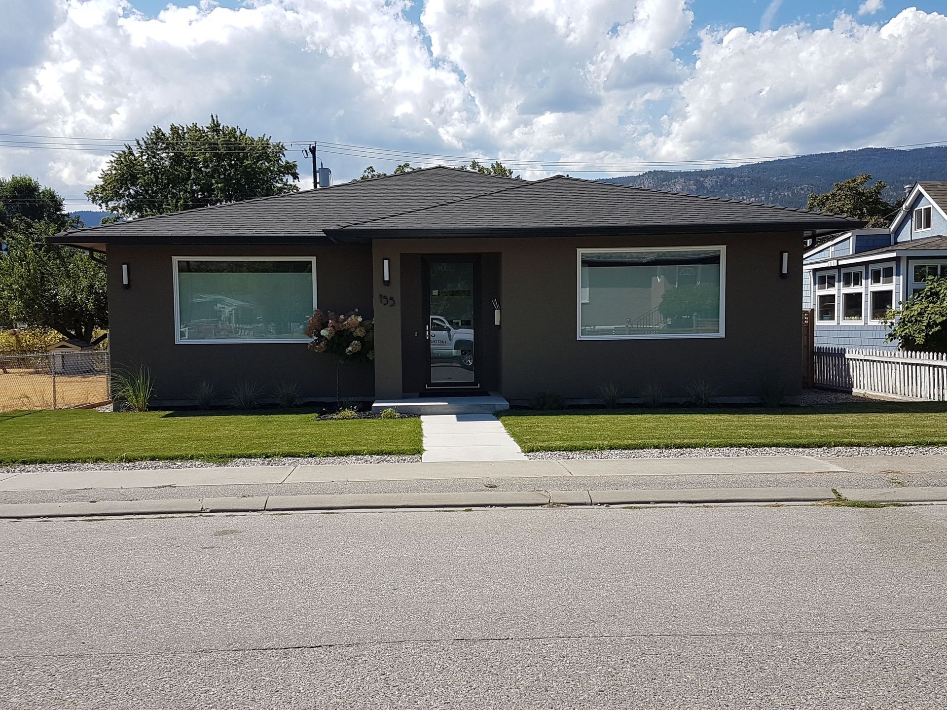 Dark gray house with a small lawn and large windows on a sunny day.