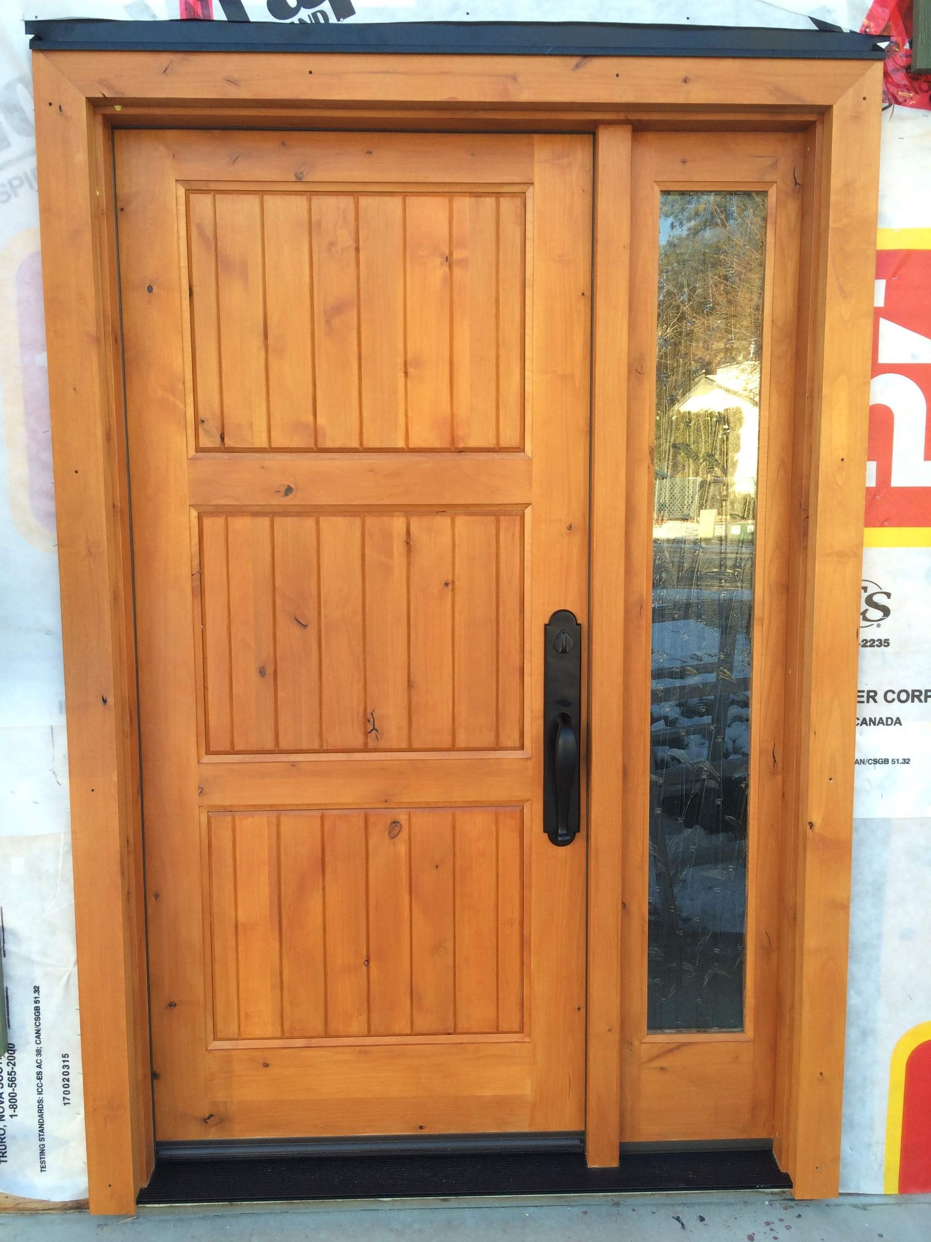 Wooden front door with sidelight. Vertical panel design with dark handle. Natural wood stain.