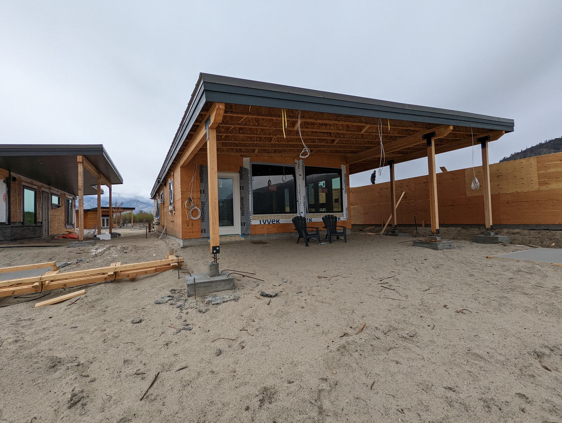 A partially constructed house with an exposed wooden frame and a dark roof under a cloudy sky.