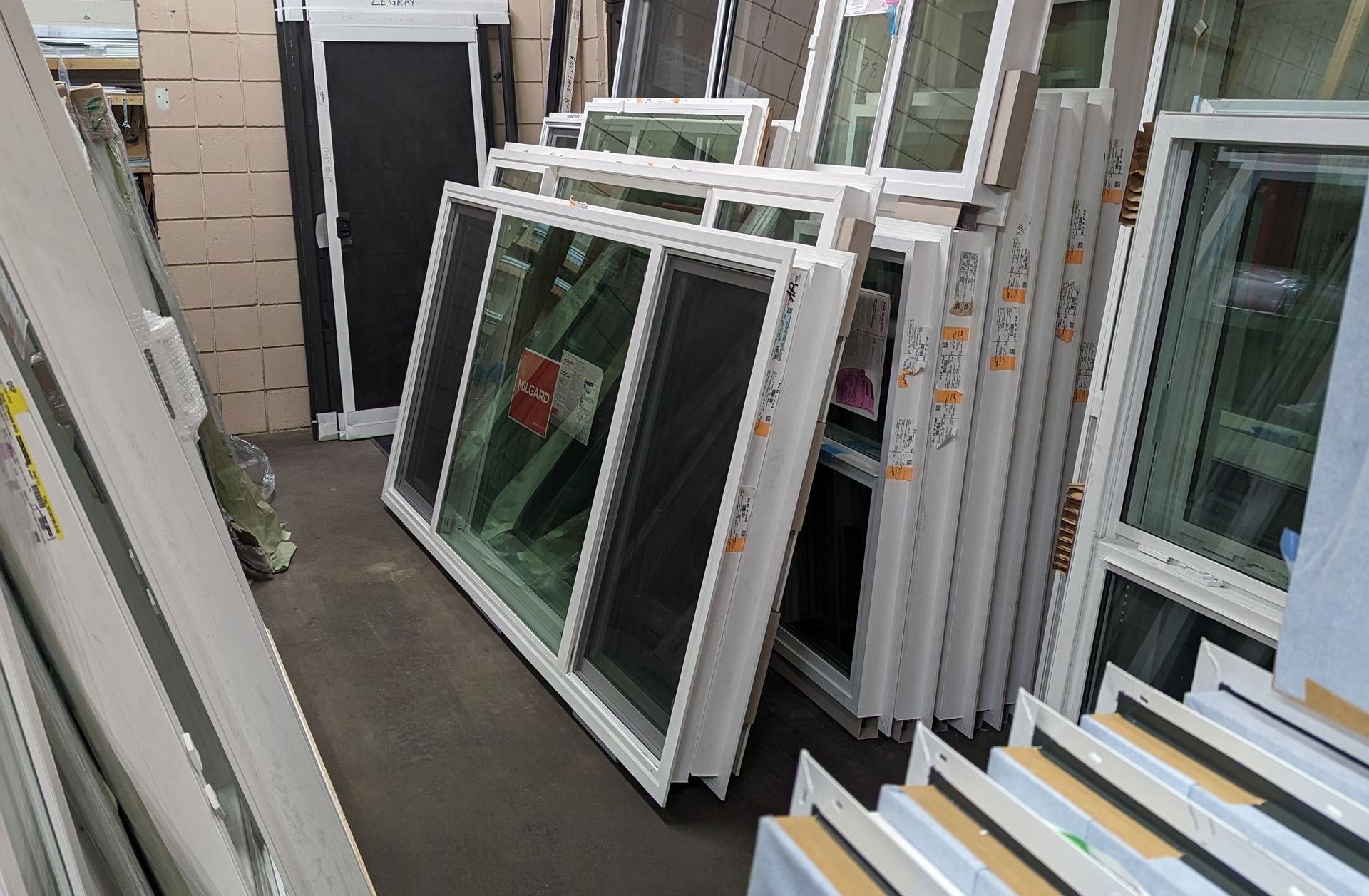 Pile of white-framed windows stacked in a storage area.