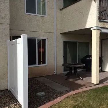 A patio with a table and a white fence in front of a house.