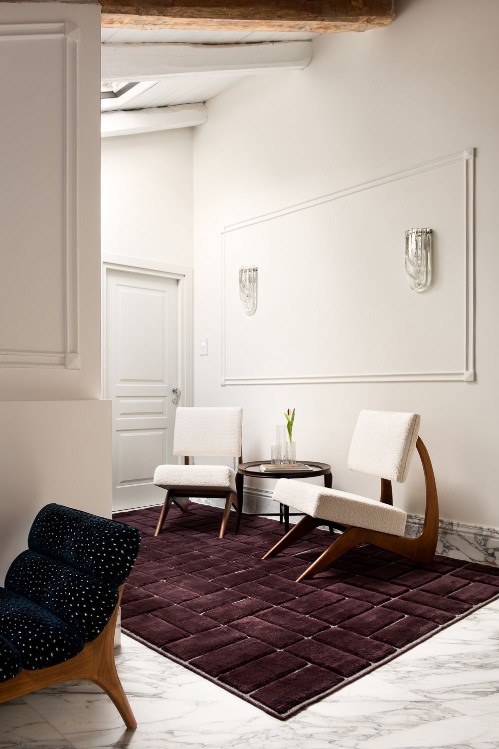 A modern interior with two white chairs, a dark rug, and a patterned blue chair against white walls.