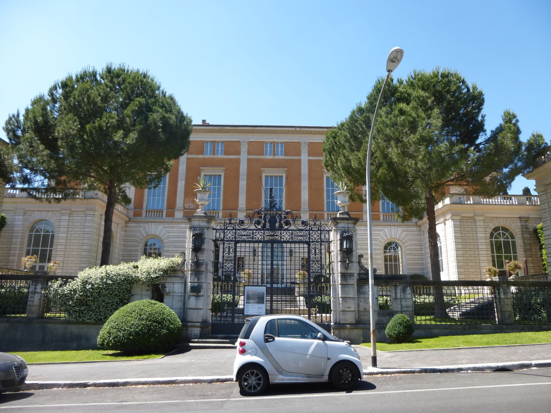Cream-colored building with black iron gate; white Smart car parked out front.