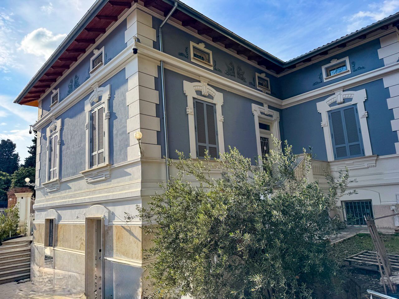 Edificio a due piani con esterni blu e finiture bianche, dotato di persiane e scala a vista.