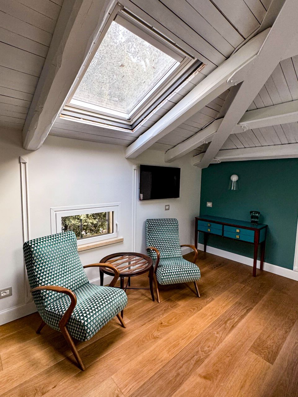 Camera accogliente con pavimenti in legno, poltrone con fantasia verde acqua e un tavolino rotondo.