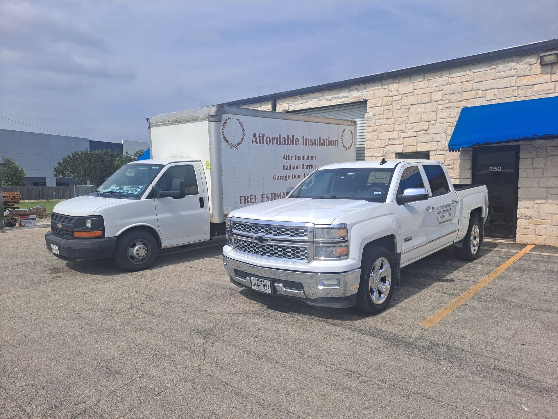 Two white trucks and a white van are parked in front of a building.