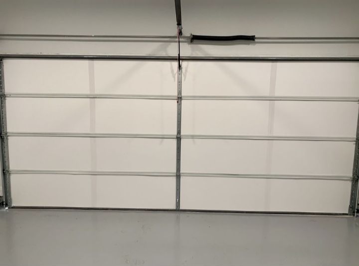 A white garage door is open in a garage with a gray floor.