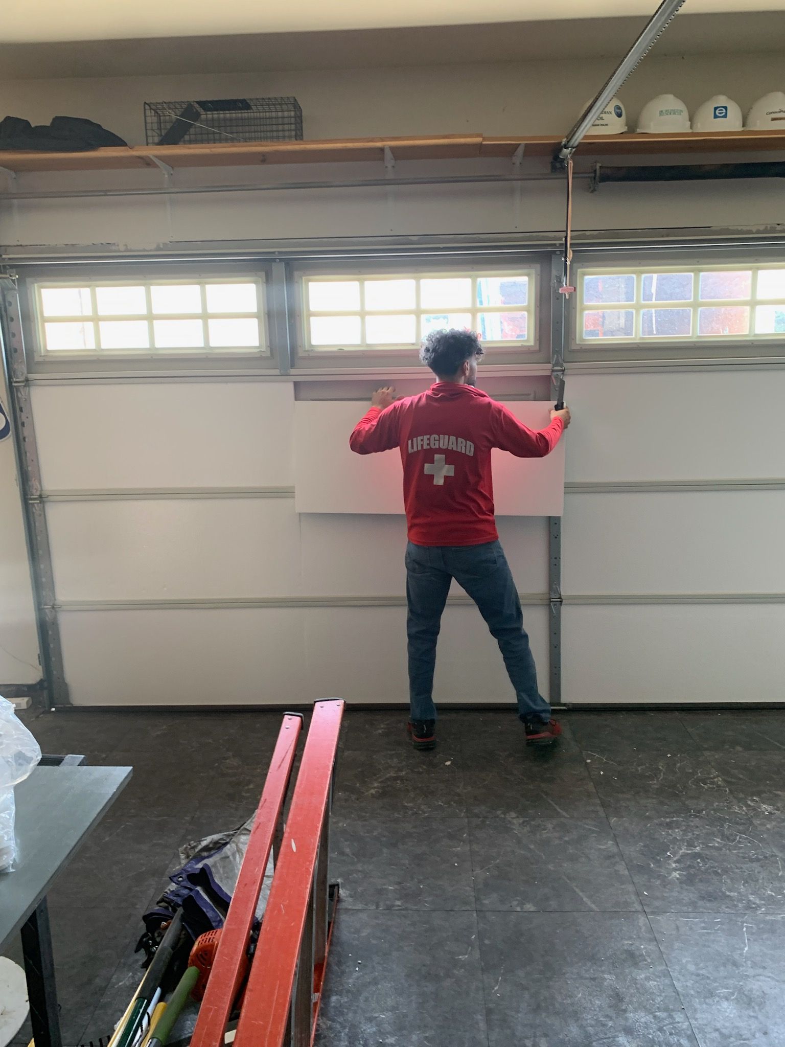 A man in a red shirt is standing in front of a garage door.
