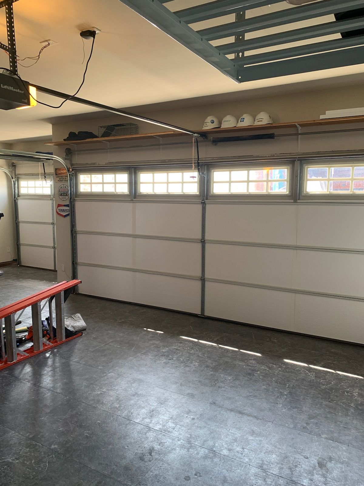 There is a ladder in the garage with a garage door open.