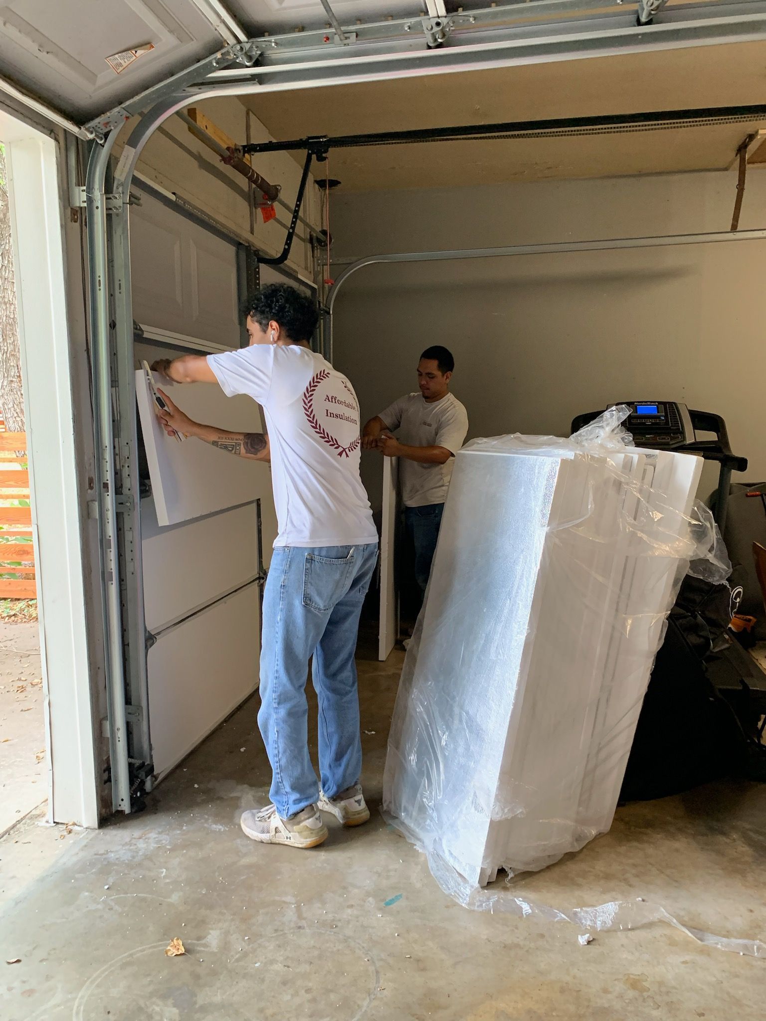 Two men are working on a garage door in a garage.