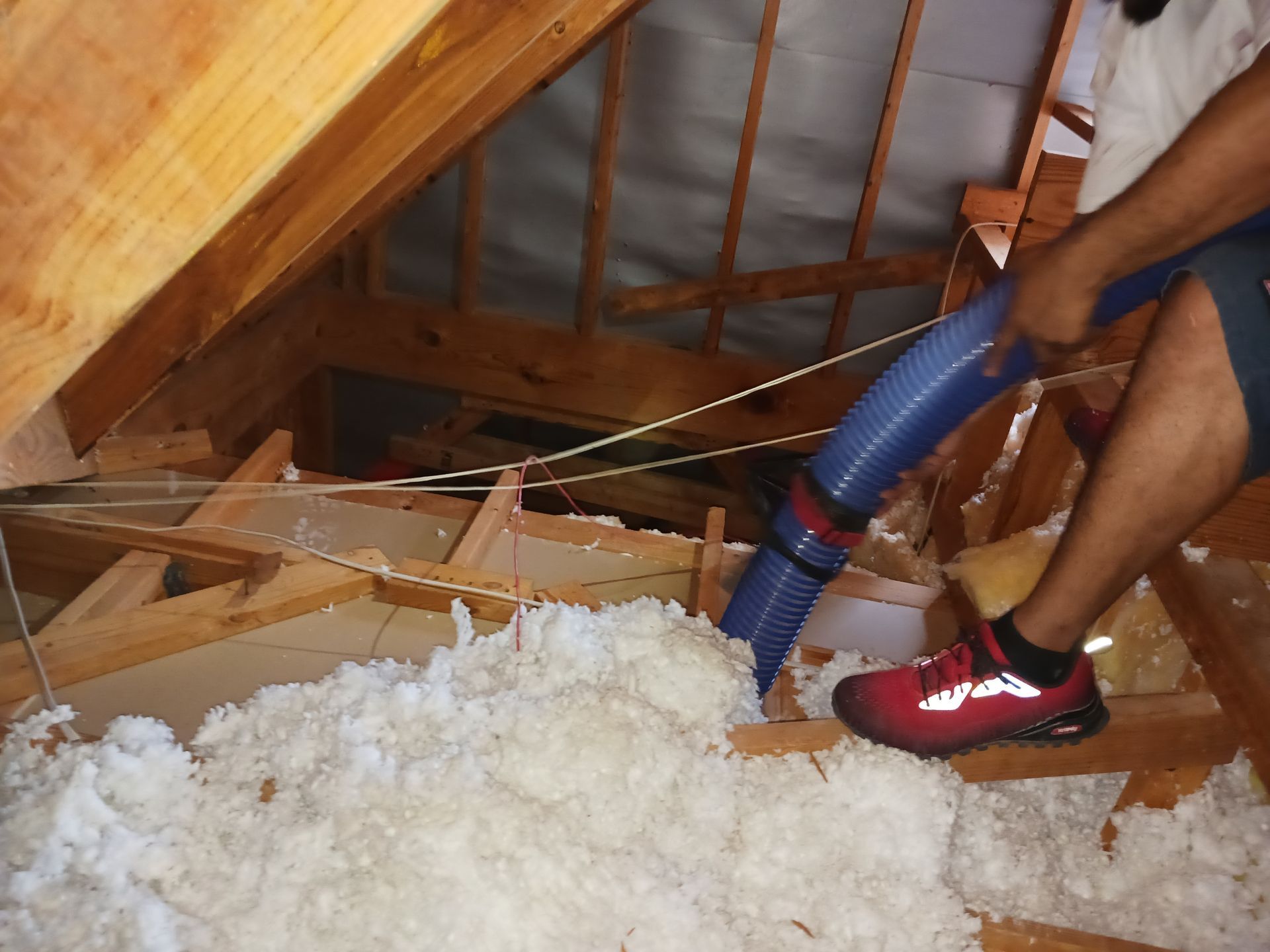 A man is using a vacuum hose to blow insulation into an attic.