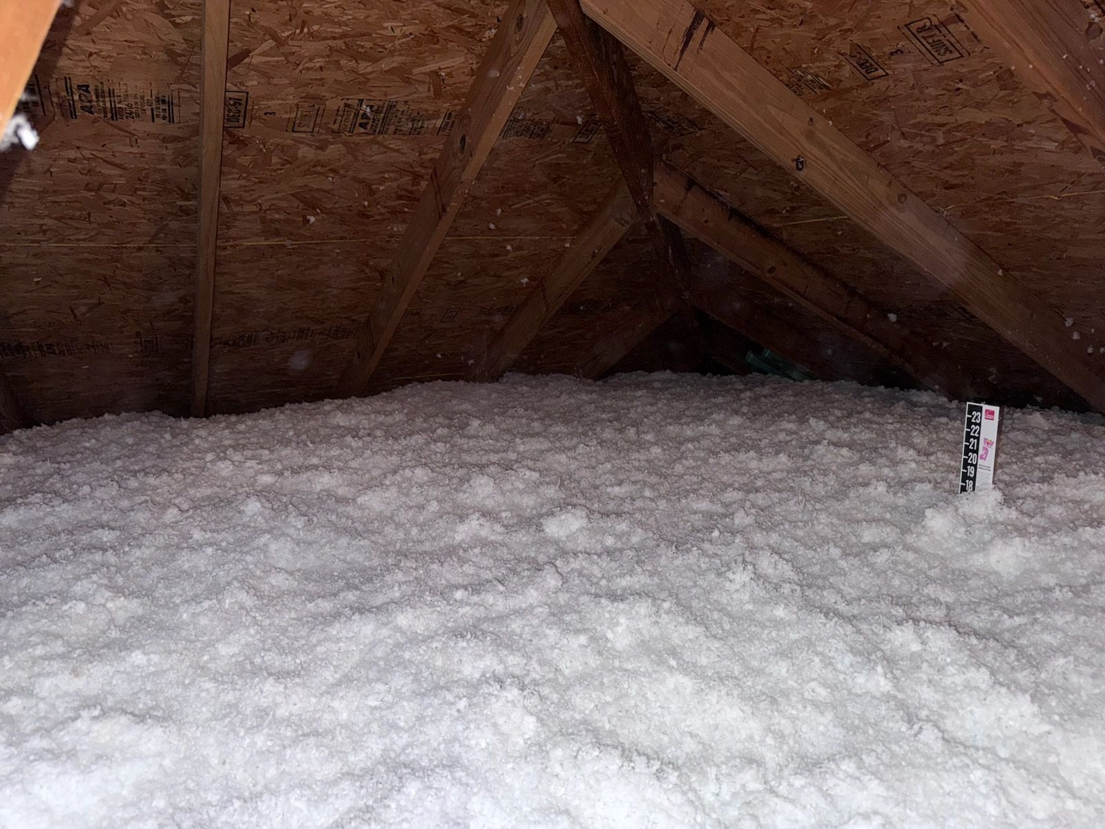 An attic filled with white insulation and a pipe.