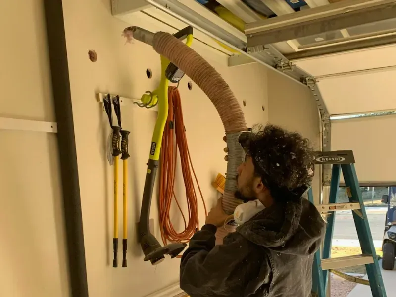 A man is using a vacuum cleaner to clean a garage door.