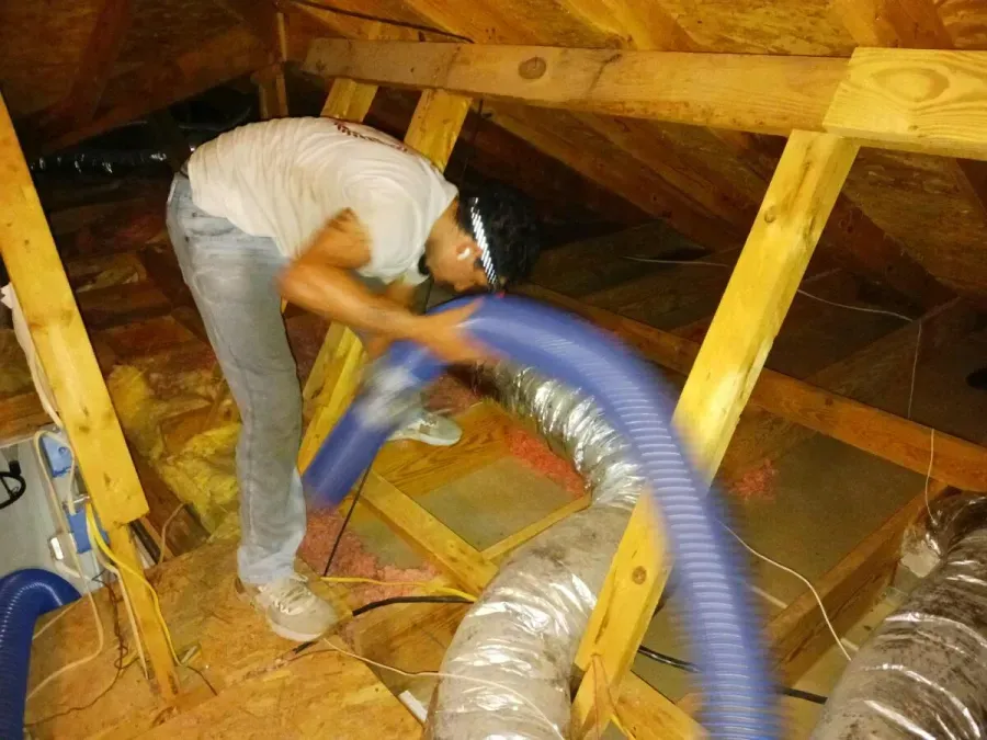 A man is working in an attic with a blue hose